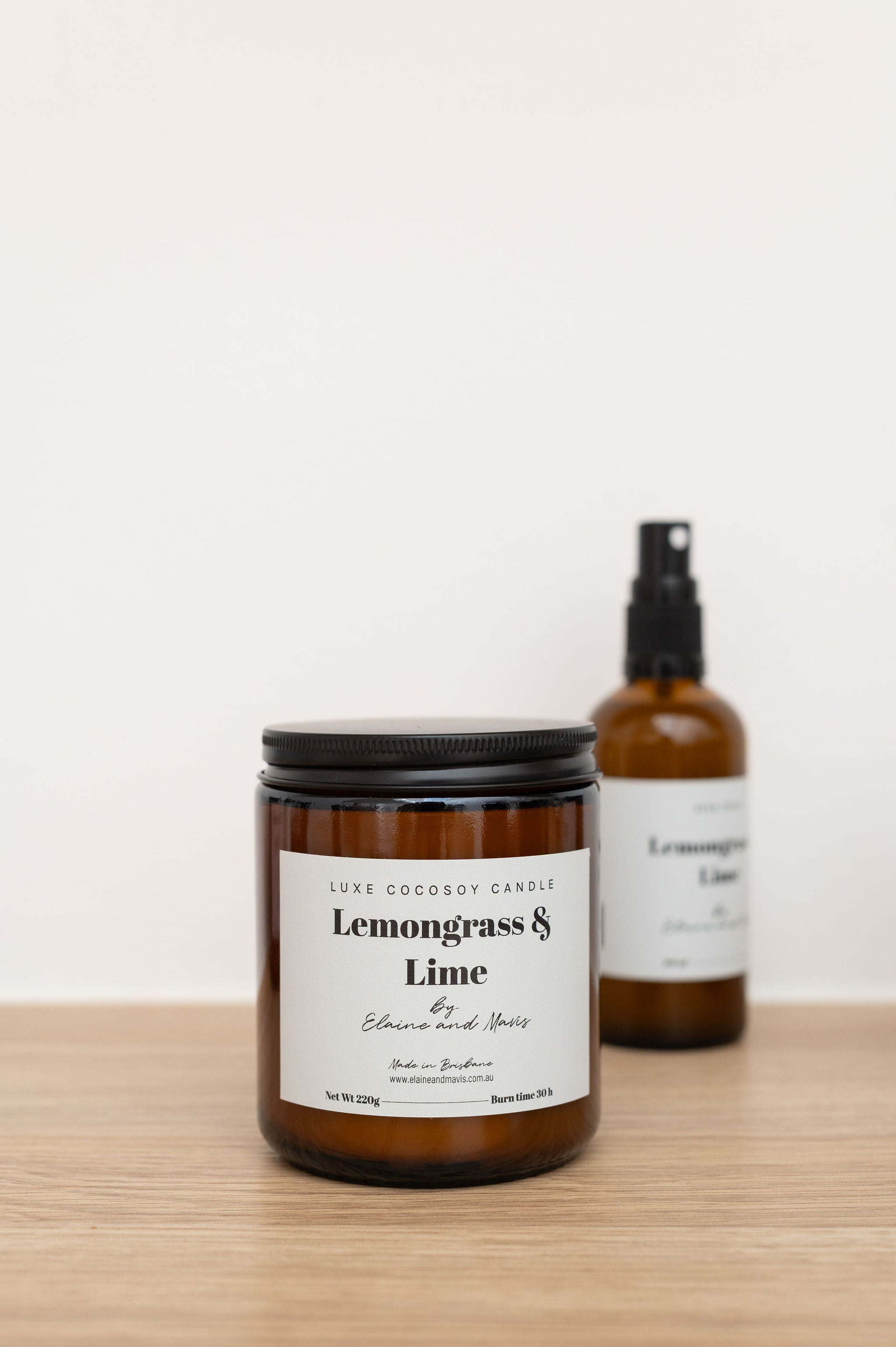 Candle and spray bottle labeled 'Lemongrass & Lime' on a wooden surface with a white background