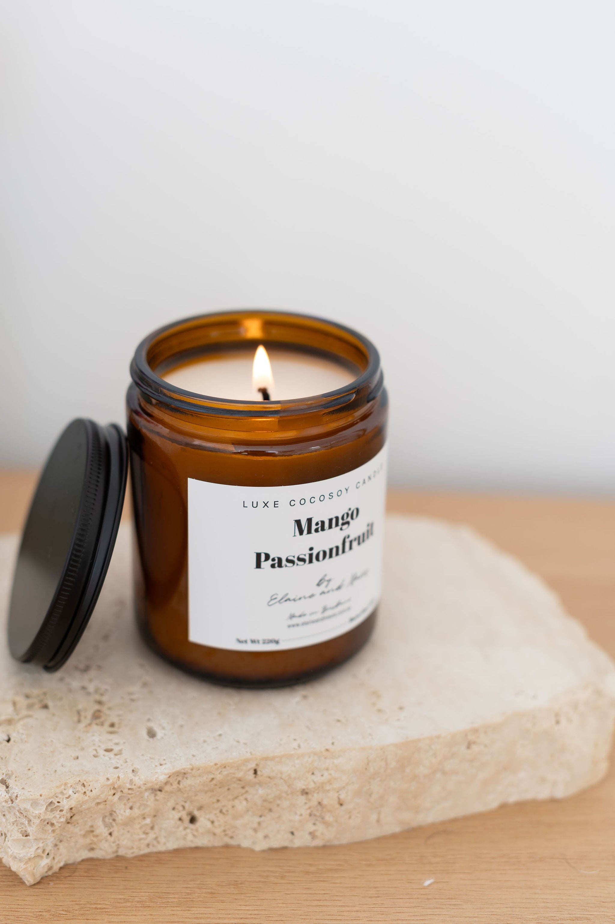 Soy Candle in an amber jar labeled 'Mango Passionfruit' on a stone surface with a white background